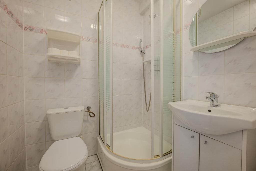 Un baño con inodoro, ducha envuelta en vidrio y lavamanos con espejo superior.