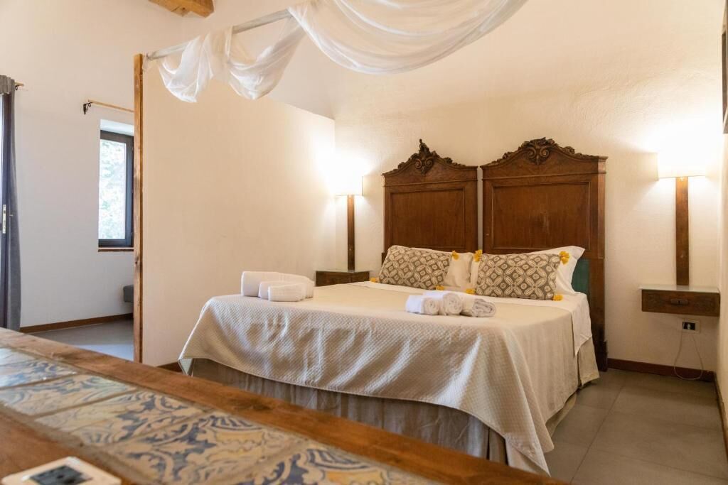 A bedroom with a large bed, two bedside tables, a nightstand, a patterned rug, and a window with curtains.