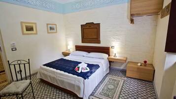 Una camera d'albergo con un letto, due comodini, una sedia e un piccolo armadietto di legno.