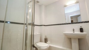 A bathroom with a glass shower enclosure, a white toilet, a white sink with a mirror above it, and a black and white tiled backsplash. - 11 Fountain Court (Falmouth)