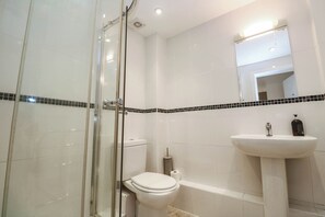 Ein Badezimmer mit einer Duschkabine aus Glas, einer weißen Toilette, einem weißen Waschbecken mit Spiegel darüber und einer schwarz-weißen Fliesenrückwand.