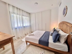 Ein Schlafzimmer mit einem hölzernen Bett, weißen Vorhängen, einem Holztisch und einer Wandleuchte.