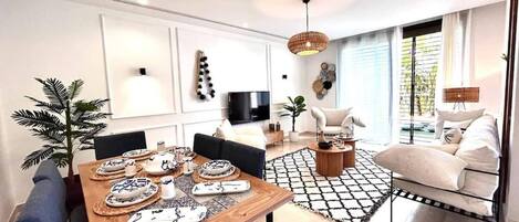 A modern living room with a dining area, a TV, and a large window.