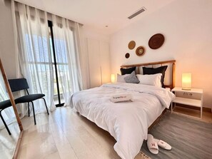 Ein Schlafzimmer mit Bett, Stuhl, Nachttisch, Lampe und einem Fenster mit Vorhängen.