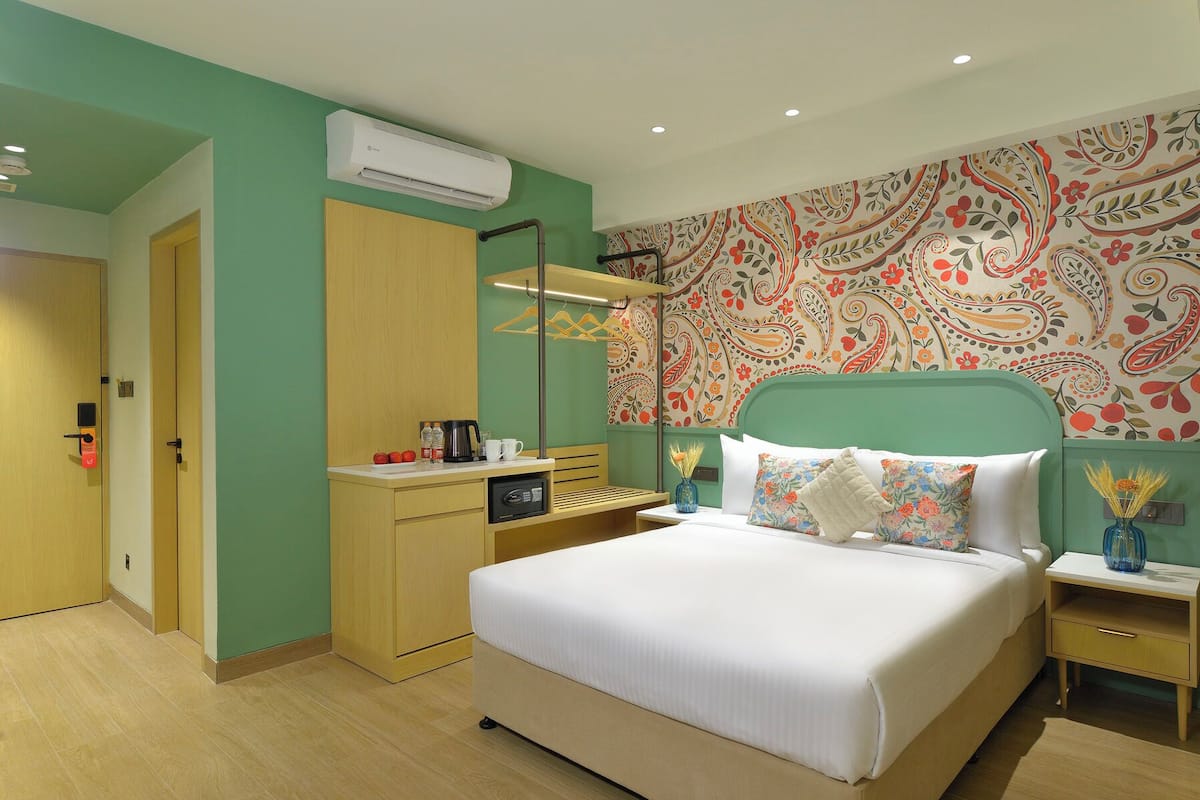 Quarto de hotel com cama, mesas de cabeceira, guarda-roupa, ar condicionado e papel de parede estampado.