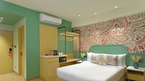 Una habitación de hotel con cama, mesitas de noche, armario, equipo de aire acondicionado y un papel tapiz estampado.