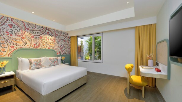 Habitación de hotel con cama, escritorio, televisor y ventana con vista a zonas verdes.