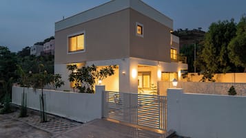 A modern two-story house with a balcony, a gated entrance, and a view of the surrounding area.