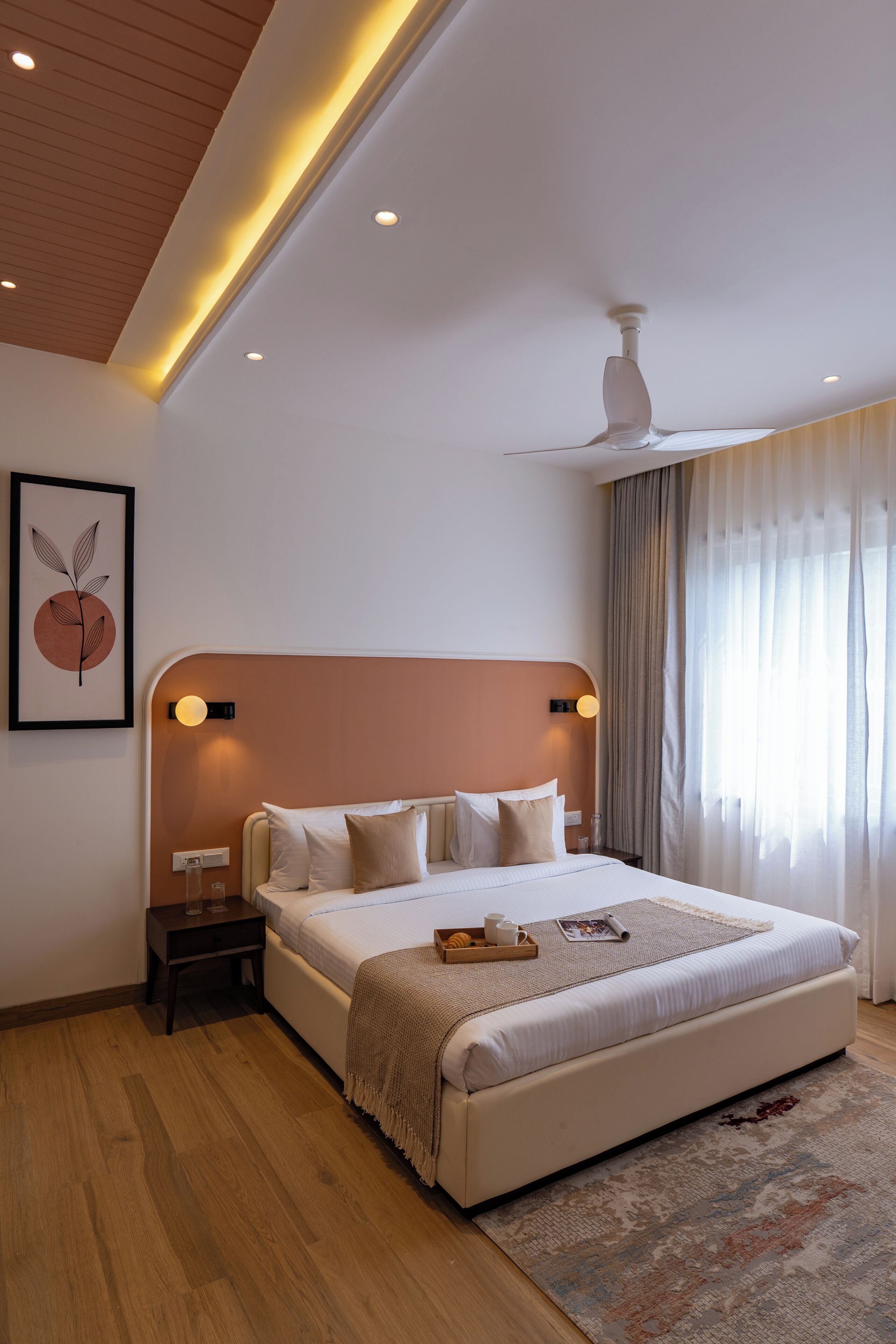 Une chambre moderne avec un grand lit, des tables de chevet, un ventilateur de plafond et une œuvre d’art encadrée au mur.