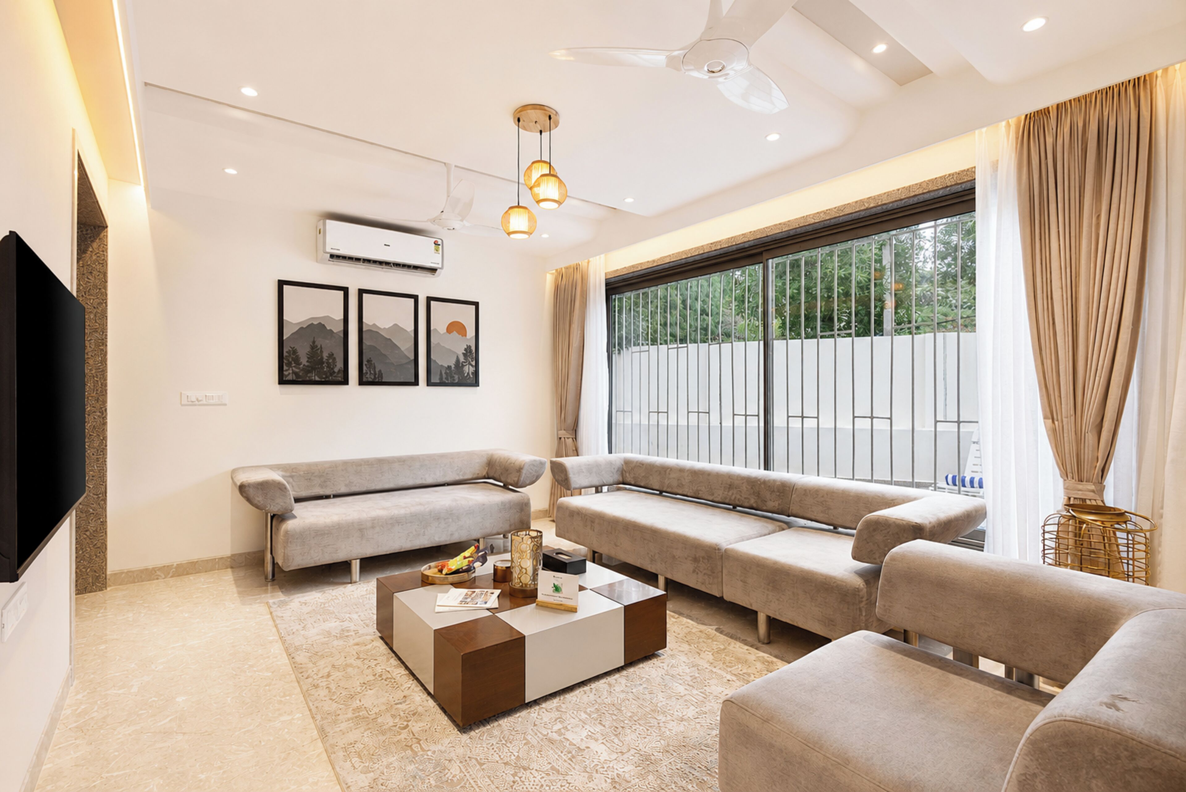 A modern living room with a flat-screen TV, a sofa set, a coffee table, and a large window with curtains.