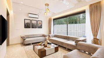 A modern living room with a flat-screen TV, a sofa set, a coffee table, and a large window with curtains.
