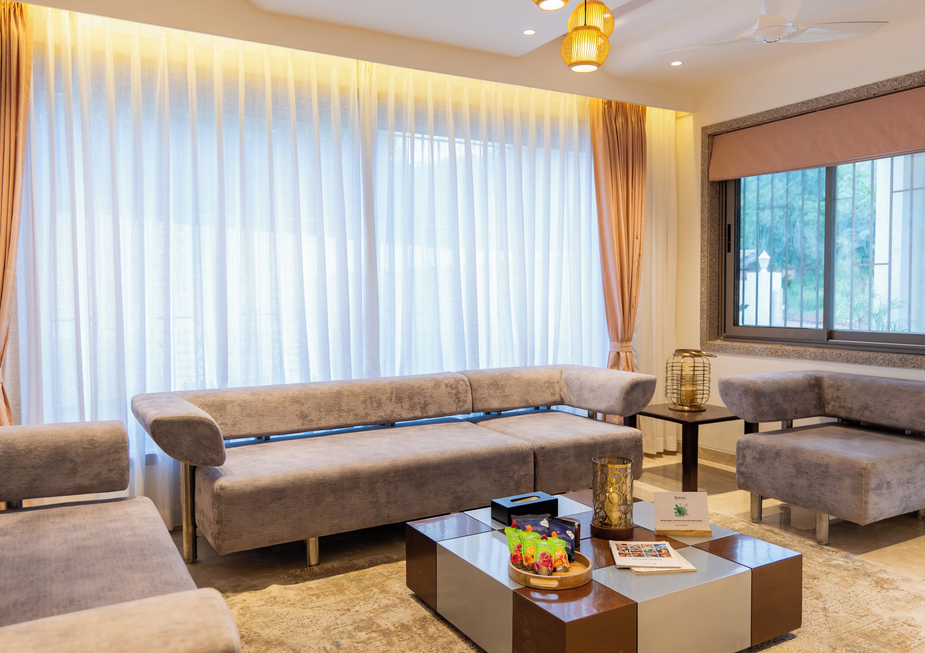 A modern living room with a sofa, armchairs, a coffee table, and a view through large windows.