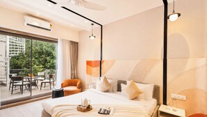 Una habitació d'hotel moderna amb un llit gran, una taula auxiliar, una tauleta de nit, una finestra amb vista a la verdura i un balcó amb mobles d'exterior.