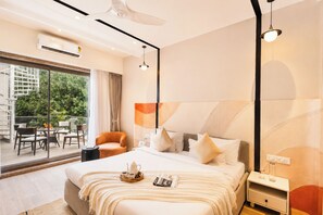 A modern hotel room with a large bed, a side table, a nightstand, a window with a view of greenery, and a balcony with outdoor furniture. - ELIVAAS Signature Shourya Aravalli 4BHK (Udaipur)
