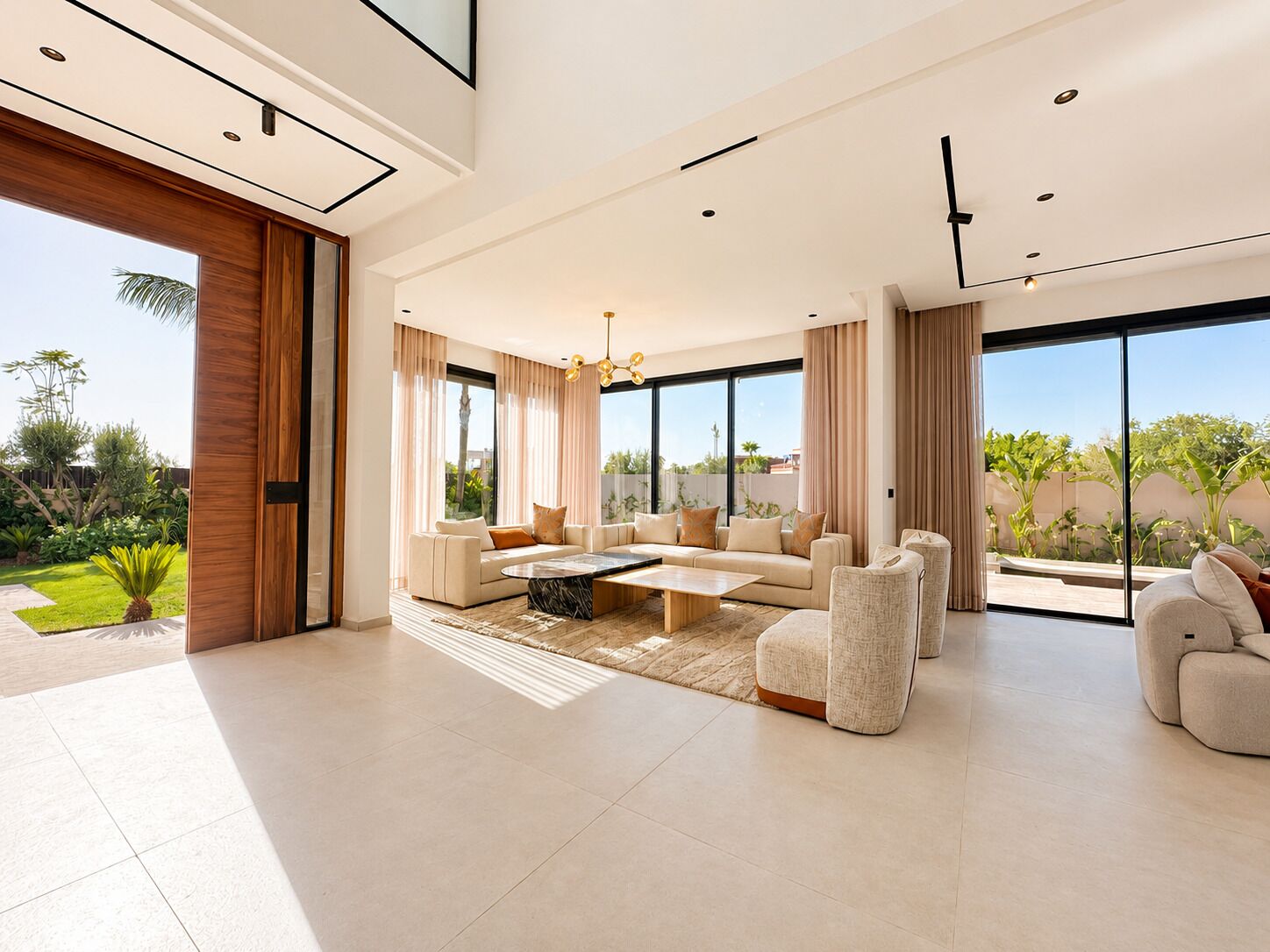 A spacious living room with a large sofa set, a coffee table, and a view of a garden through large windows.