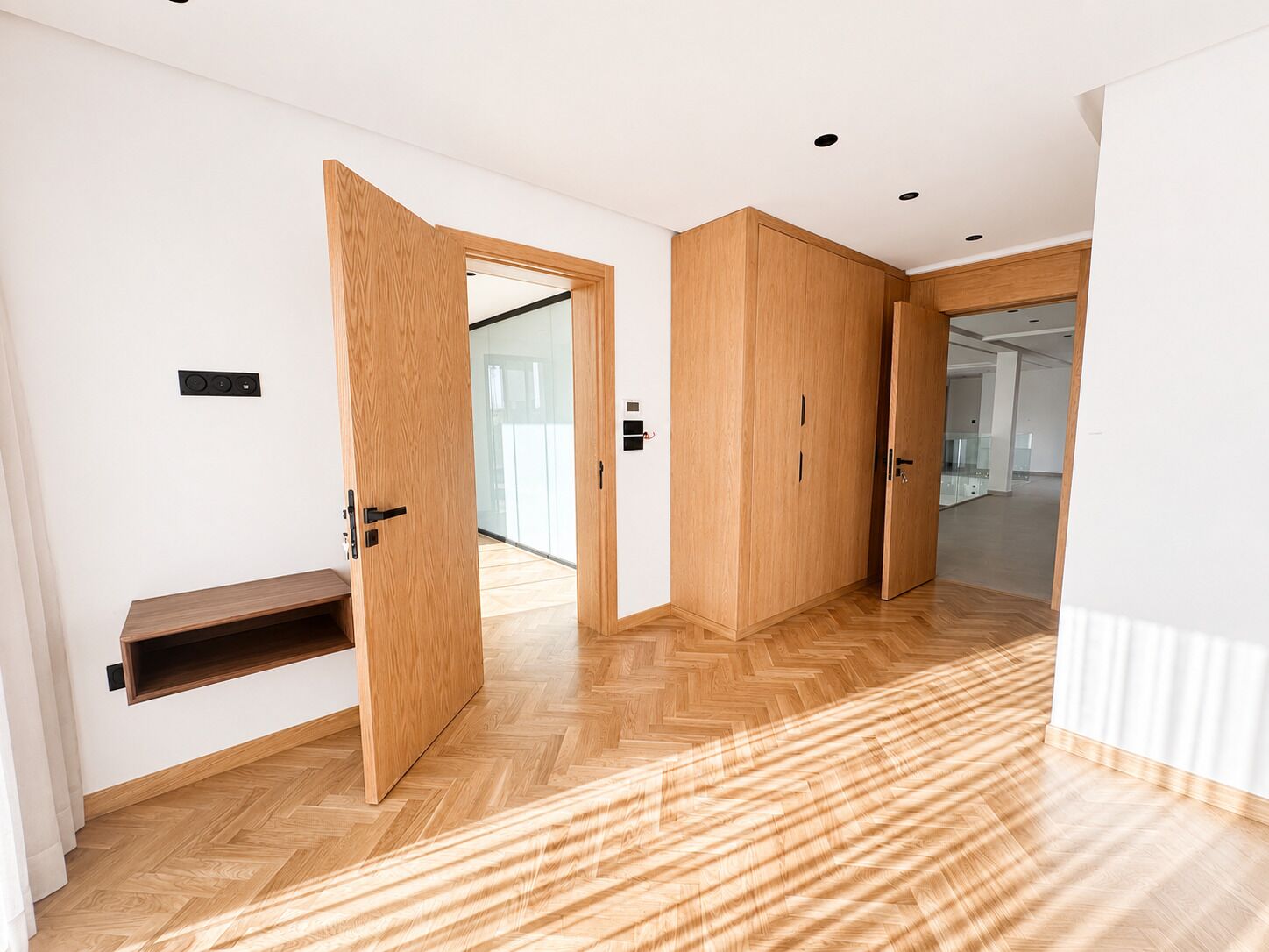 Un pasillo con piso de madera, un banco y una puerta que da a otra habitación.