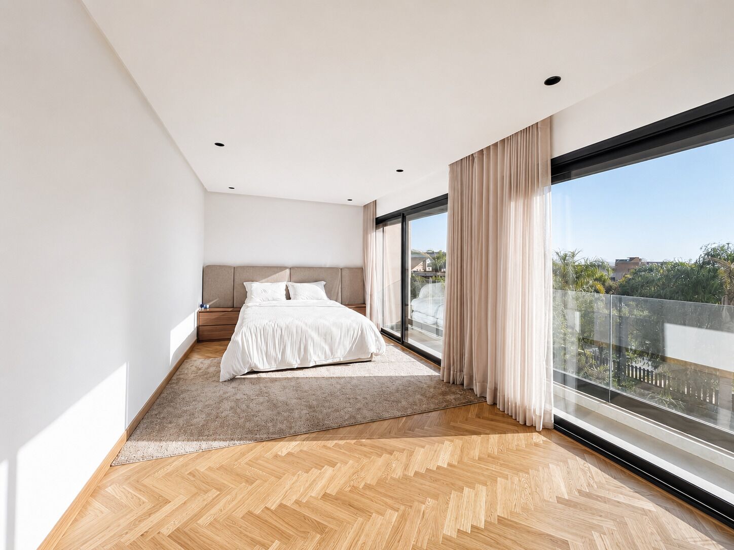 A modern bedroom with a large bed, a view through a sliding glass door, and a herringbone wood floor.