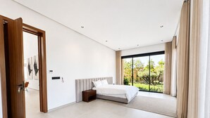 A modern bedroom with a large bed, a wooden door, and a view of a garden through a sliding glass door. - Villa contemporaine - Golf d'Amelkis - Ascenseur et hammam (Marrakech)