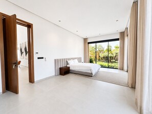 Ein modernes Schlafzimmer mit einem großen Bett, einer Holztür und Blick auf einen Garten durch eine Schiebetür.