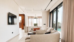 A modern living room with a curved sofa, a coffee table, and a large window with curtains. - Villa contemporaine - Golf d'Amelkis - Ascenseur et hammam (Marrakech)