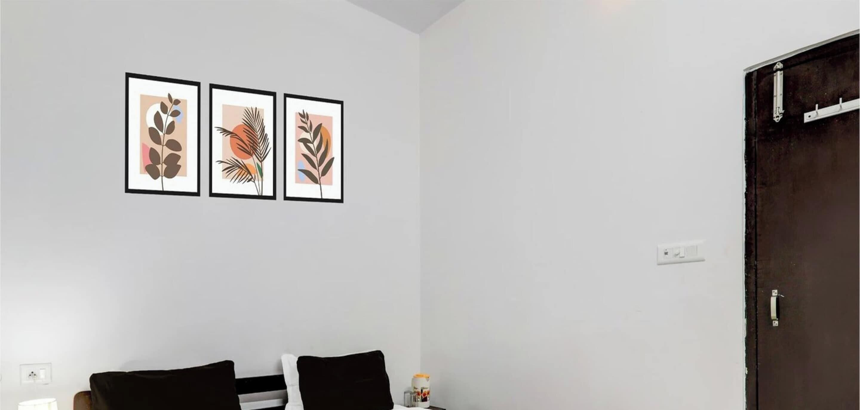 A room with a bed, a nightstand, and a door. There are three framed pictures on the wall.