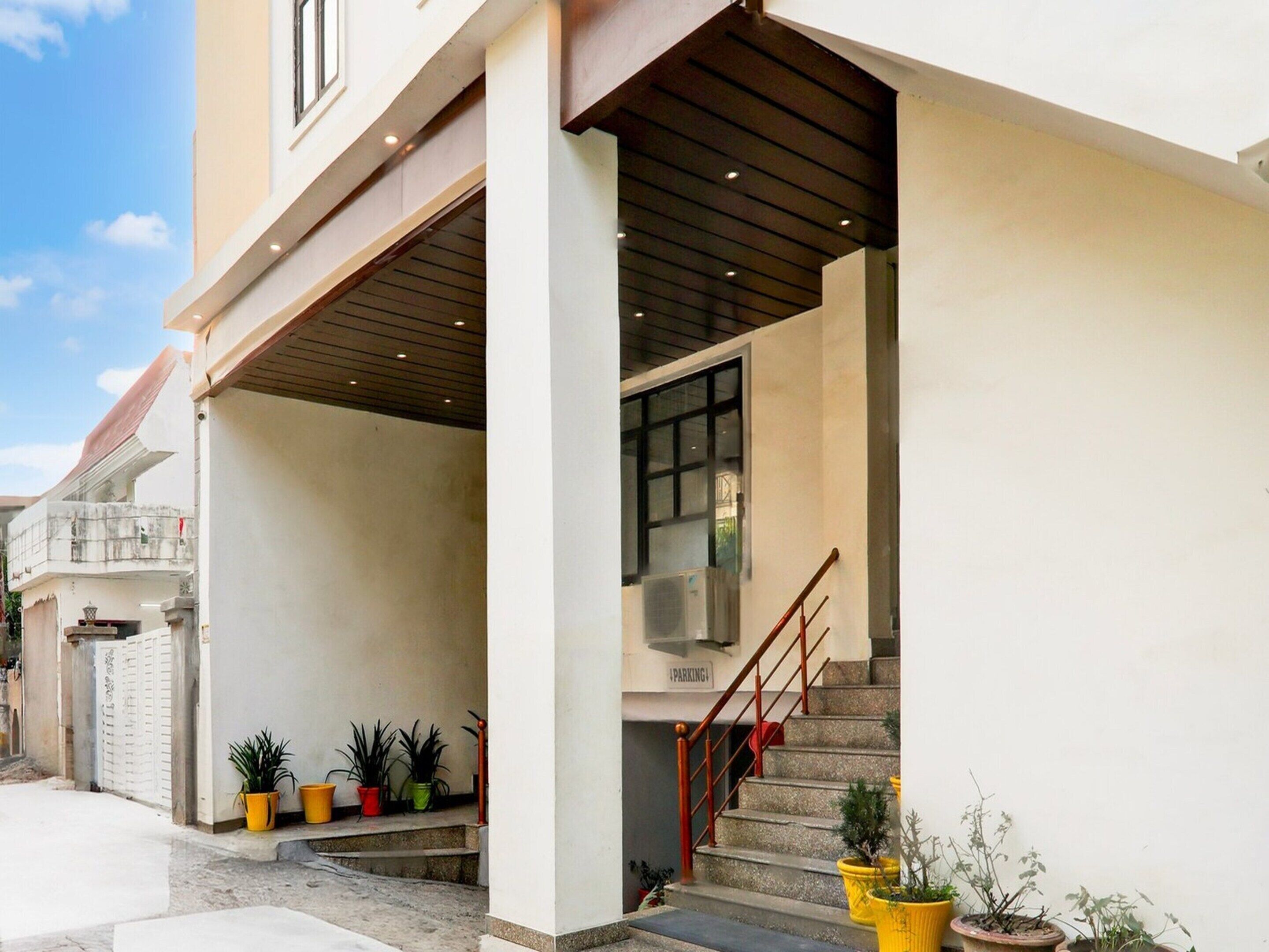 A building entrance with a staircase, a sign indicating parking, and potted plants.