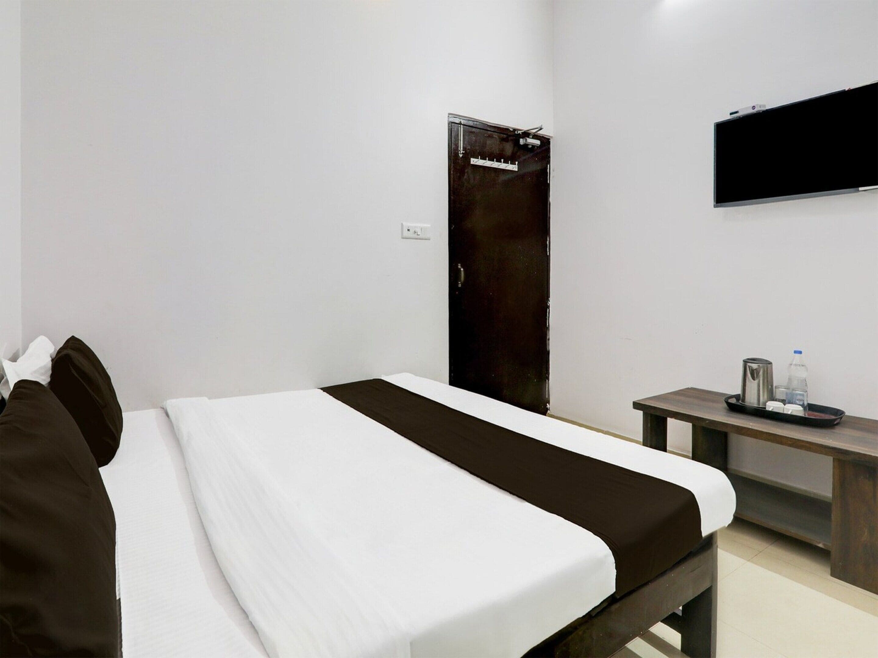 A hotel room with a bed, a bedside table with a tray, a wall-mounted TV, and a door.