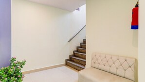 Una escalera que sube a un piso superior, un sofá color beige y una planta en maceta con flores rosadas.