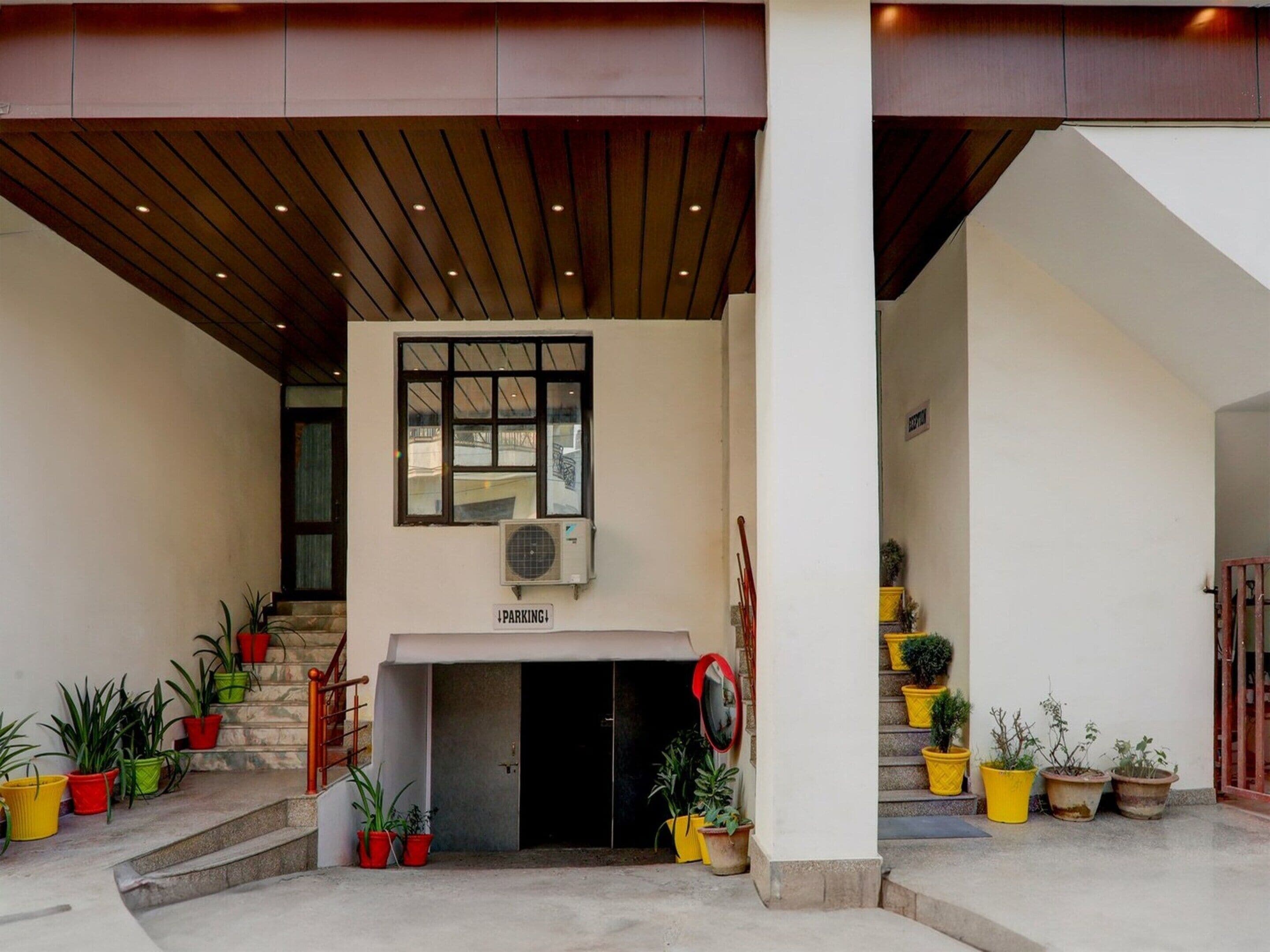 A building entrance with a staircase, a sign indicating parking, and potted plants.