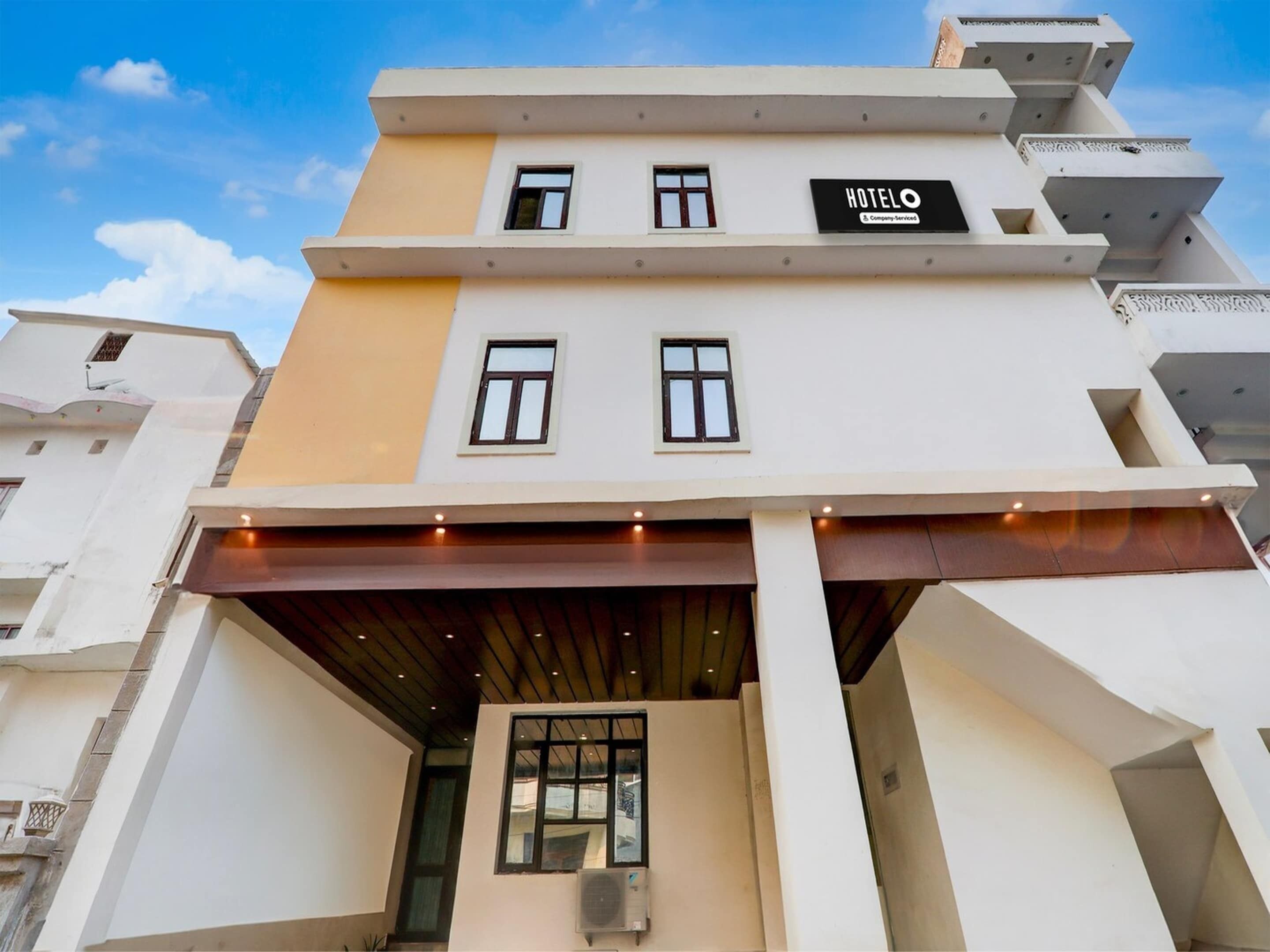 A hotel named 'HOTELO' with a modern architectural design, featuring a flat facade, multiple windows, and a covered entrance area.