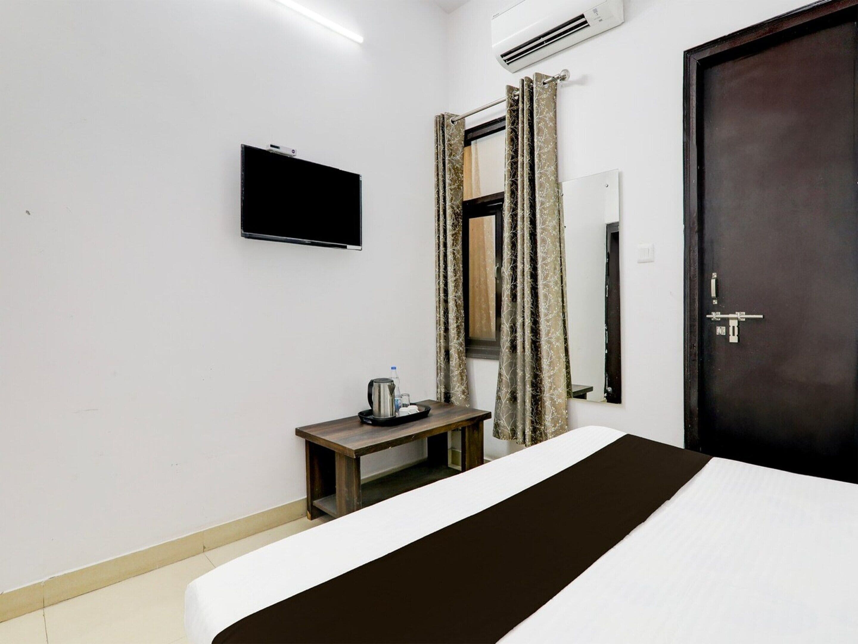 Ein Hotelzimmer mit einem Bett, einem Nachttisch mit Wasserkocher, einem flachbildschirmfernseher an der Wand und einer Tür mit Schloss.