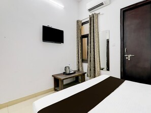 A hotel room with a bed, a bedside table with a kettle, a flat-screen TV mounted on the wall, and a door with a lock. - Deluxe Hotel Parijat (Lucknow)