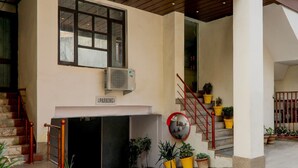 Entrada de un edificio con escaleras, un cartel que indica estacionamiento y plantas en macetas.