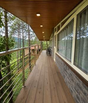 A wooden deck with a railing, a table with chairs, and large windows.