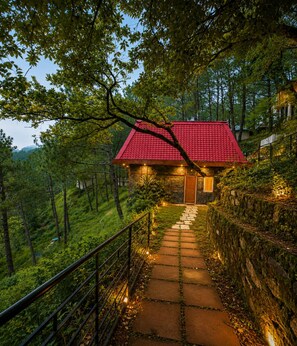 A house with a red roof, surrounded by lush greenery and a stone pathway leading to the entrance.