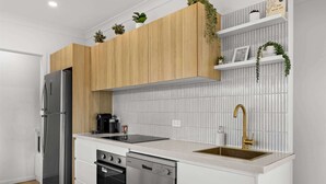 Une cuisine moderne avec des meubles en bois, un réfrigérateur en acier inoxydable, un lave-vaisselle et un évier doté d’un robinet doré.