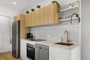 A modern kitchen with wooden cabinets, a stainless steel refrigerator, a dishwasher, and a sink with a gold faucet.