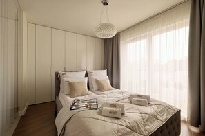 A modern bedroom with a bed, a bedside table, a hanging light fixture, and a window with curtains. - 154 sqm | Chmielna 63 Penthouse | 3 Bedrooms | AC (Gdańsk)