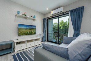 A modern living room with a large window, a flat-screen TV, a sofa, a white entertainment unit, and a balcony with a chair. - The Title Residencies Naiyang-Electricity & Water Included-E414 (Thalang/Sakhu)