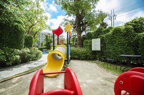A playground with a slide and climbing structures, surrounded by greenery and a paved path. - The Title Residencies Naiyang-Electricity & Water Included-E414 (Thalang/Sakhu)