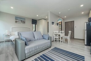 Ein modernes Wohnzimmer mit grauem Sofa, einem Esstisch mit Stühlen, einer Küchenzeile mit Kühlschrank und einem Streifenmuster-Teppich.