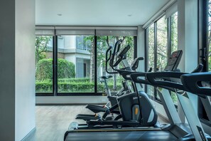 Ein Fitnessstudio mit Trainingsgeräten und großen Fenstern, die Blick auf Grünflächen und Gebäude gewähren.
