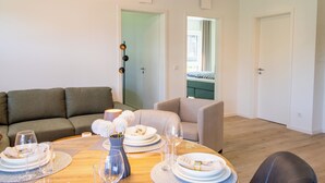 A modern living room with a dining area, featuring a sofa, a chair, a dining table set with plates, glasses, and a vase with flowers. - Coastal Lodge 33/1 - Just a step from the sea. Sauna. Patio. Garden. (Tossens)
