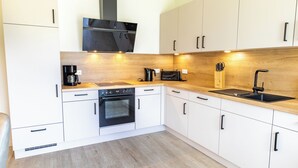 A modern kitchen with white cabinets, a black oven, a coffee maker, and a sink. - Coastal Lodge 33/1 - Just a step from the sea. Sauna. Patio. Garden. (Tossens)