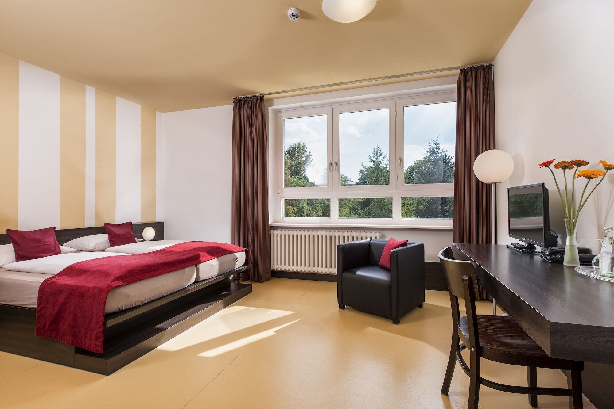 Ein Hotelzimmer mit einem Bett, einem Schreibtisch, einem Stuhl, einem Heizkörper und einem Fenster mit Vorhängen.