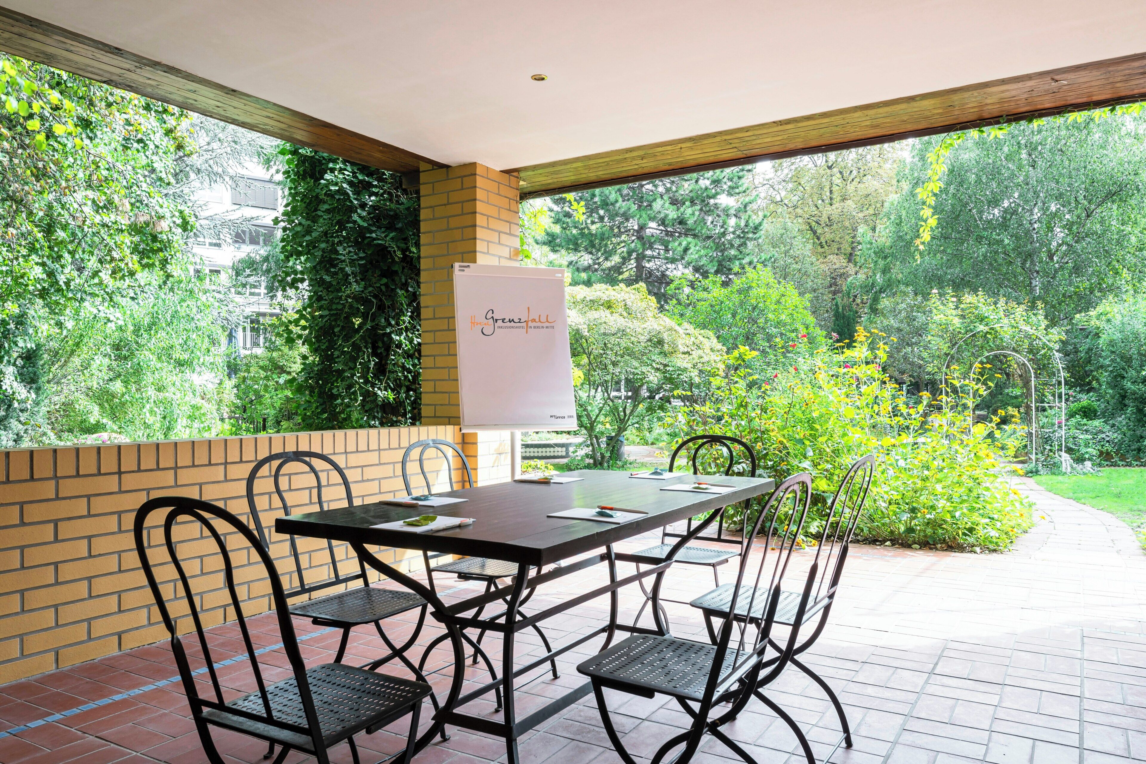 A patio area with a table and chairs, a whiteboard, and a view of a garden.
