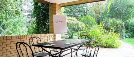 A patio area with a table and chairs, a whiteboard, and a view of a garden.