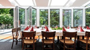 Een restaurant met grote ramen, houten stoelen en gedekte tafels.