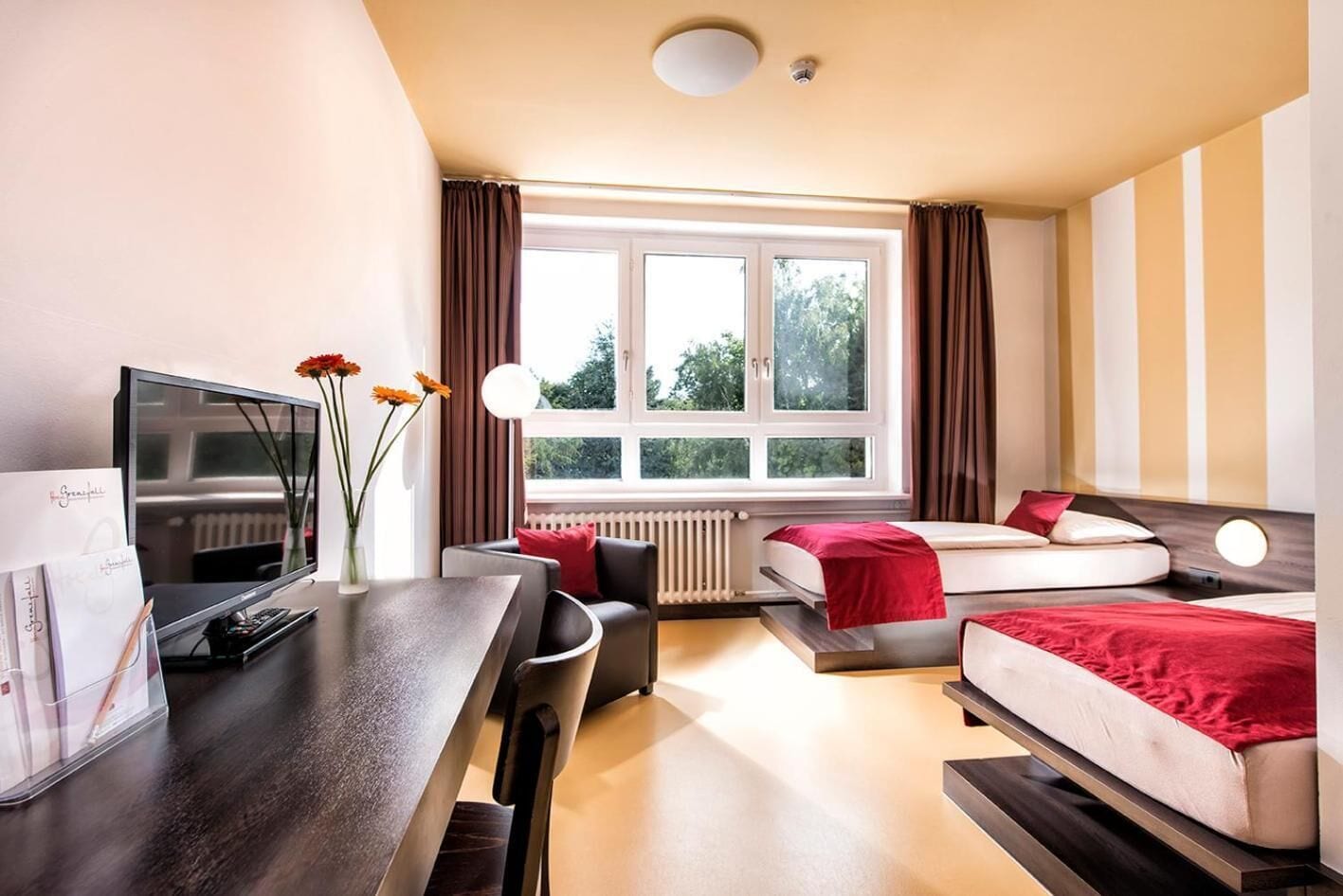 A hotel room with a TV, a desk, a chair, a sofa, and a bed.