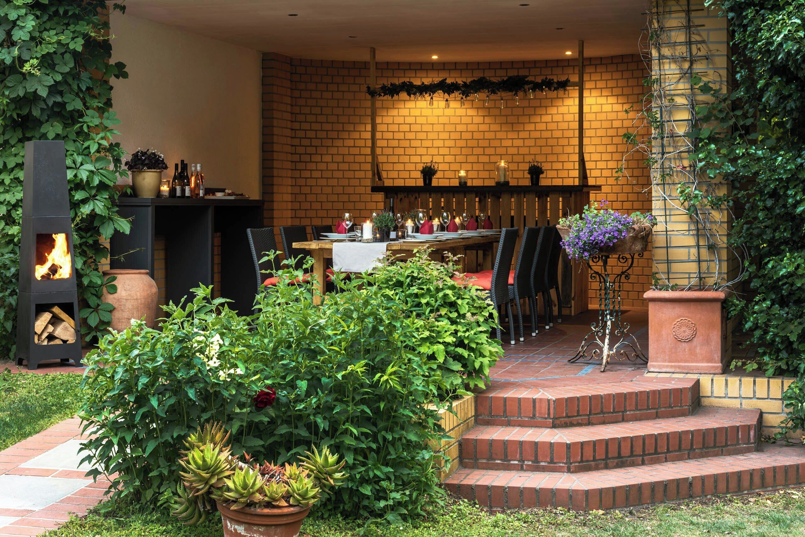 An outdoor patio with a brick wall, a fire pit, and a table set for dining.